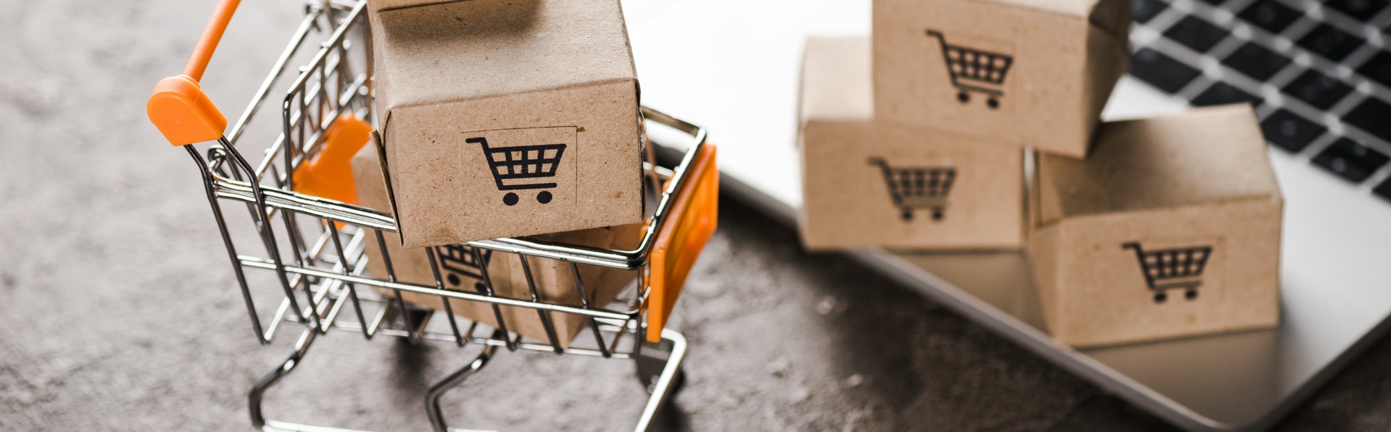 Shopping cart with small carton boxes near laptop, e-commerce concept. Tips For Small eCommerce Businesses.