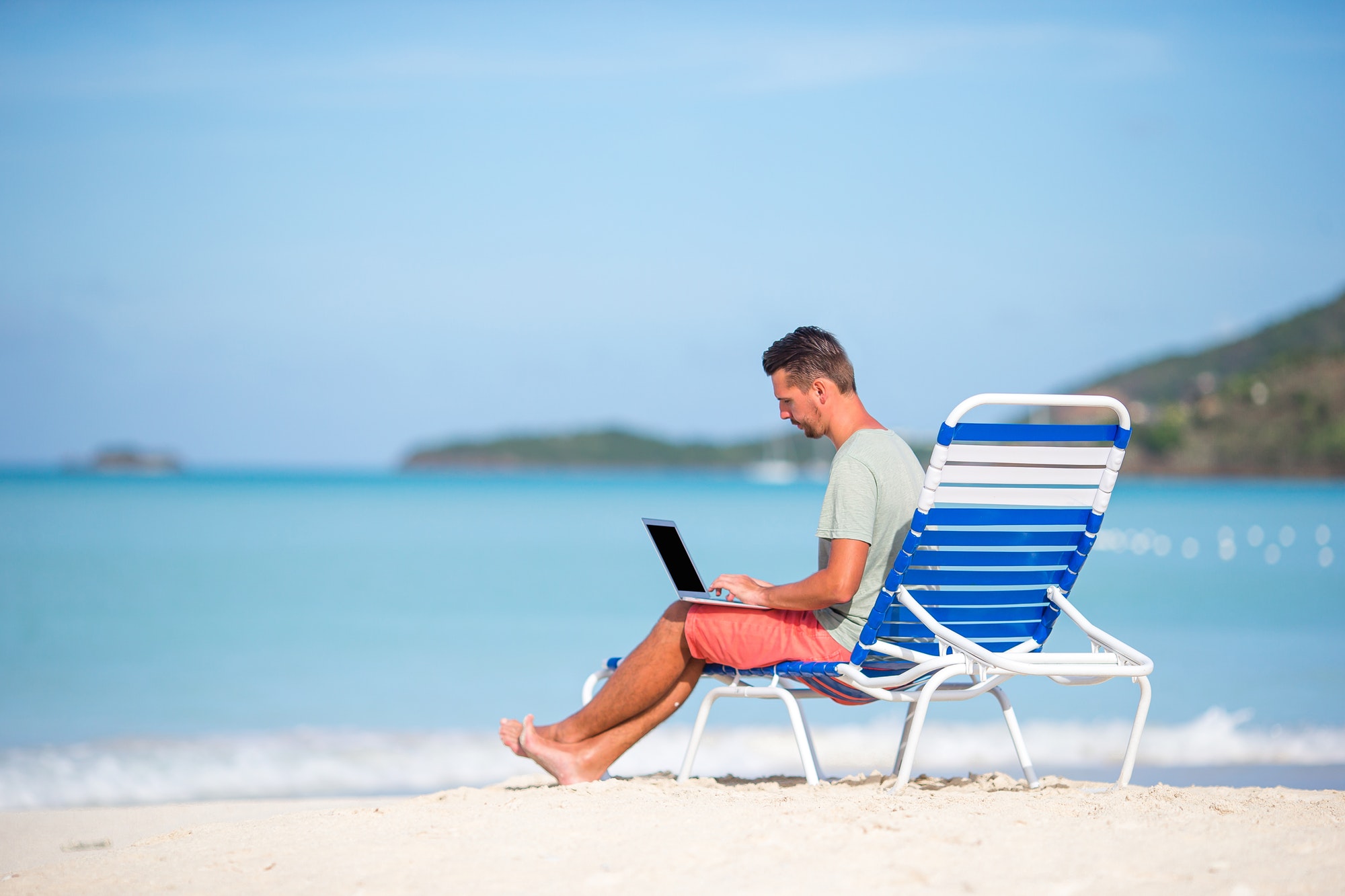 Young man with tablet working remotely from a beach.