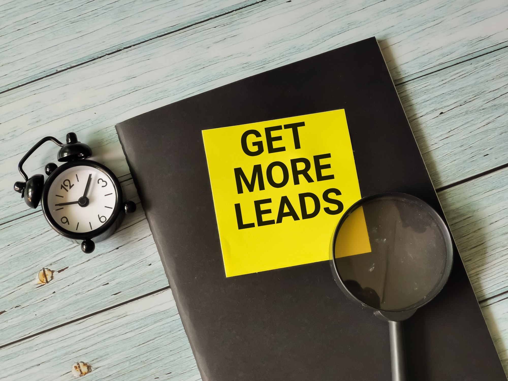 Phrase get more leads written on sticky note with alarm clock,magnifying glass and book. Lead generation software.