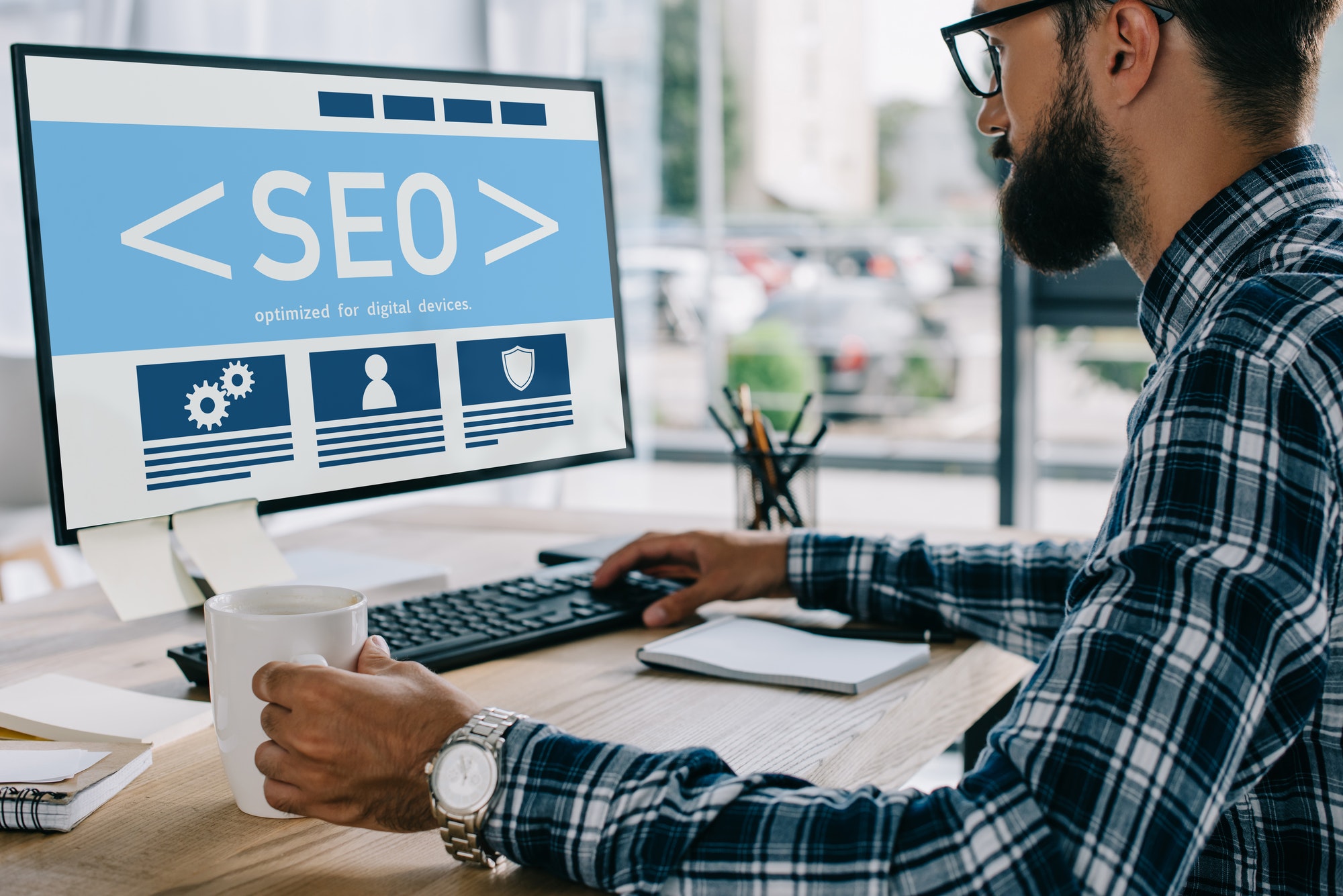 young successful developer sitting at workplace with SEO sign on computer screen