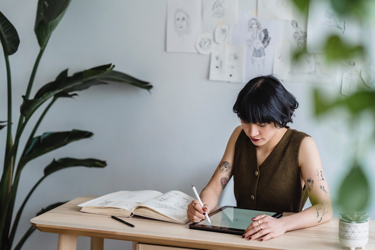 A woman using a tablet and a notebook on a desk.