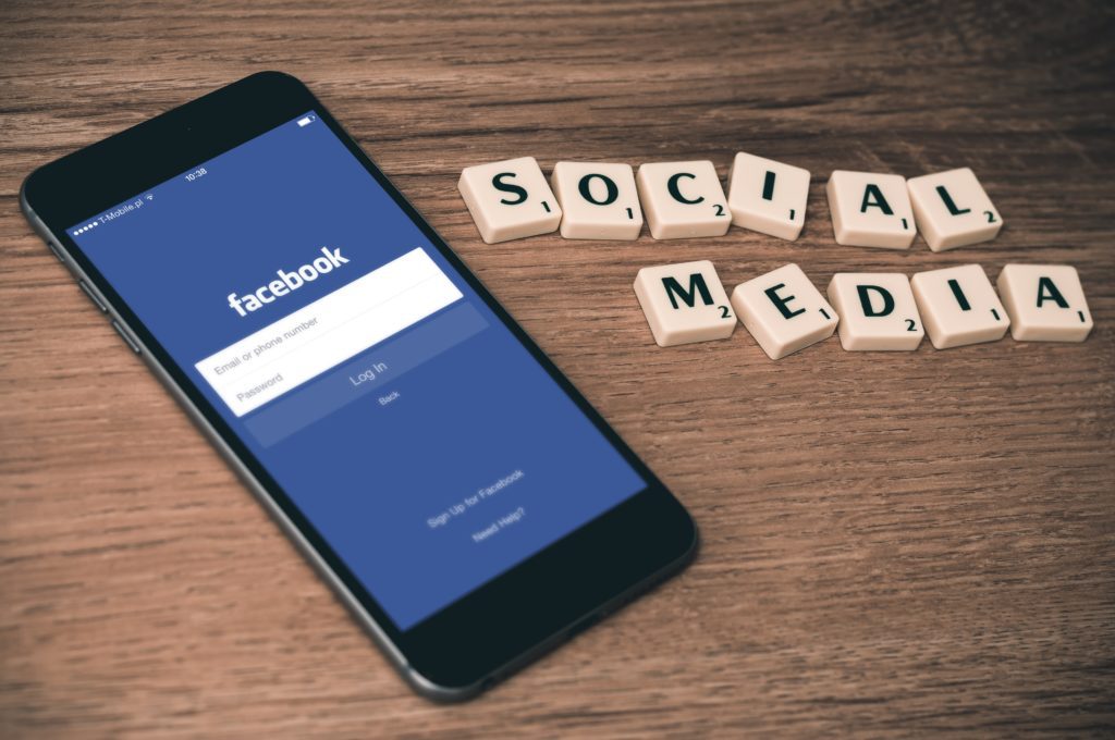 A smartphone with facebook open next to scrabble pieces spelling out "social media"
