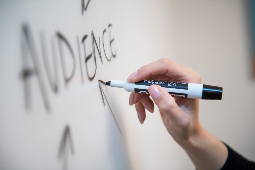 A person writing the word "audience" on a white board.
