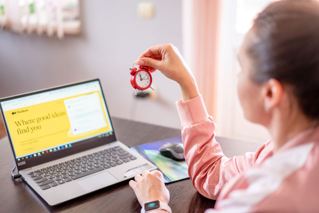 A woman working on a laptop while holding a small clock