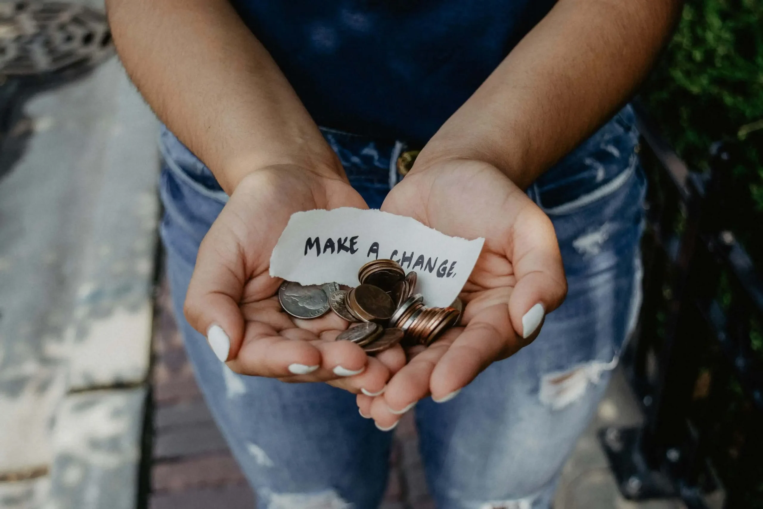 A person with a handful of coins and a note that says "make a change"
